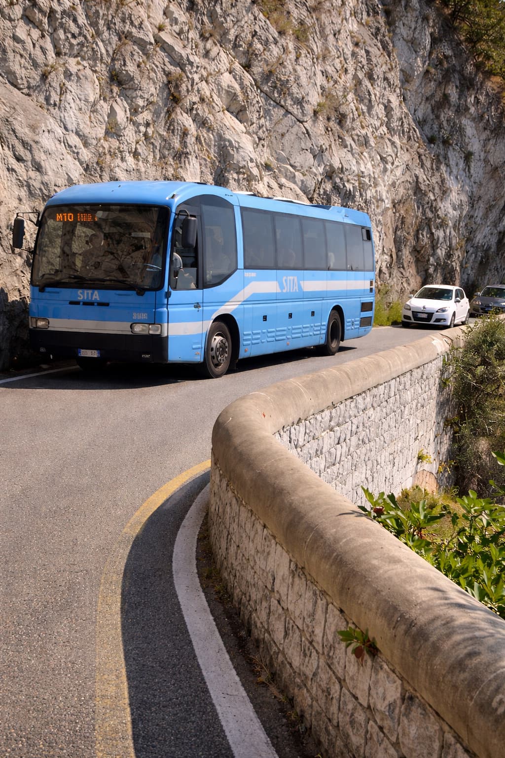 SITA bus navigating a narrow curve on the Amalfi Coast road with stone wall and cliff face