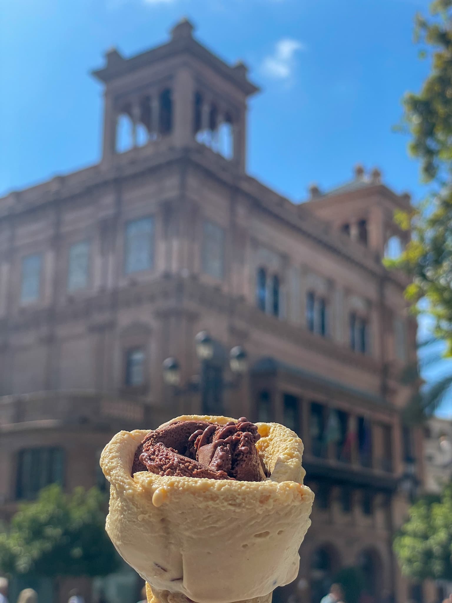 Ice cream cone held up in front of a historic building in Seville, Spain