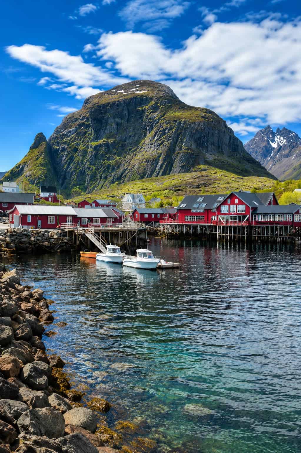 Reine village Lofoten Islands Norway — red rorbuer fishing cabins on rocky islets with Reinebringen mountain reflected in the fjord