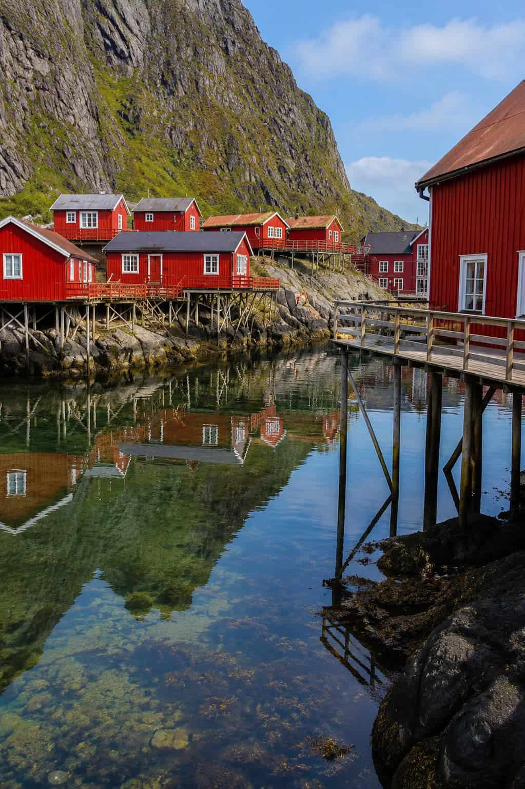 Rorbuer cabin on the waterfront Lofoten Islands Norway — traditional red wooden fishing cabin on stilts over the fjord with mountain backdrop