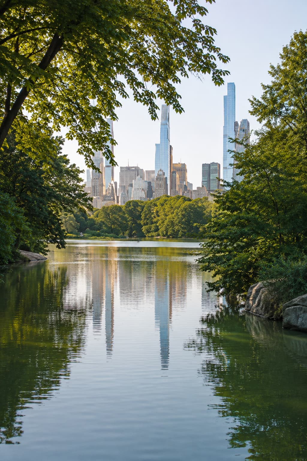Central Park lake in summer with the Manhattan skyline framed by green trees, New York