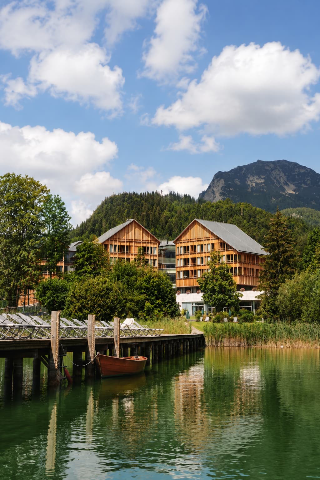 Wooden lakeside wellness hotel and jetty backed by alpine forest and mountains in Austria