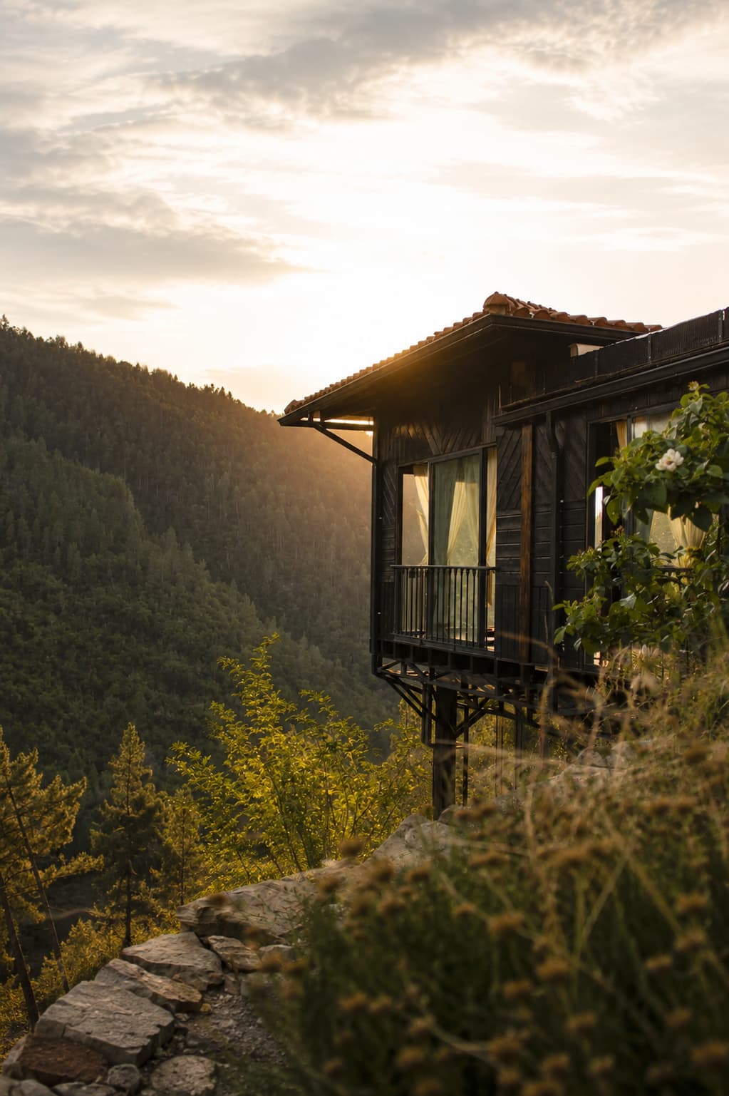 Dark-timber retreat cabin on a forested hillside at golden hour, overlooking a wooded valley