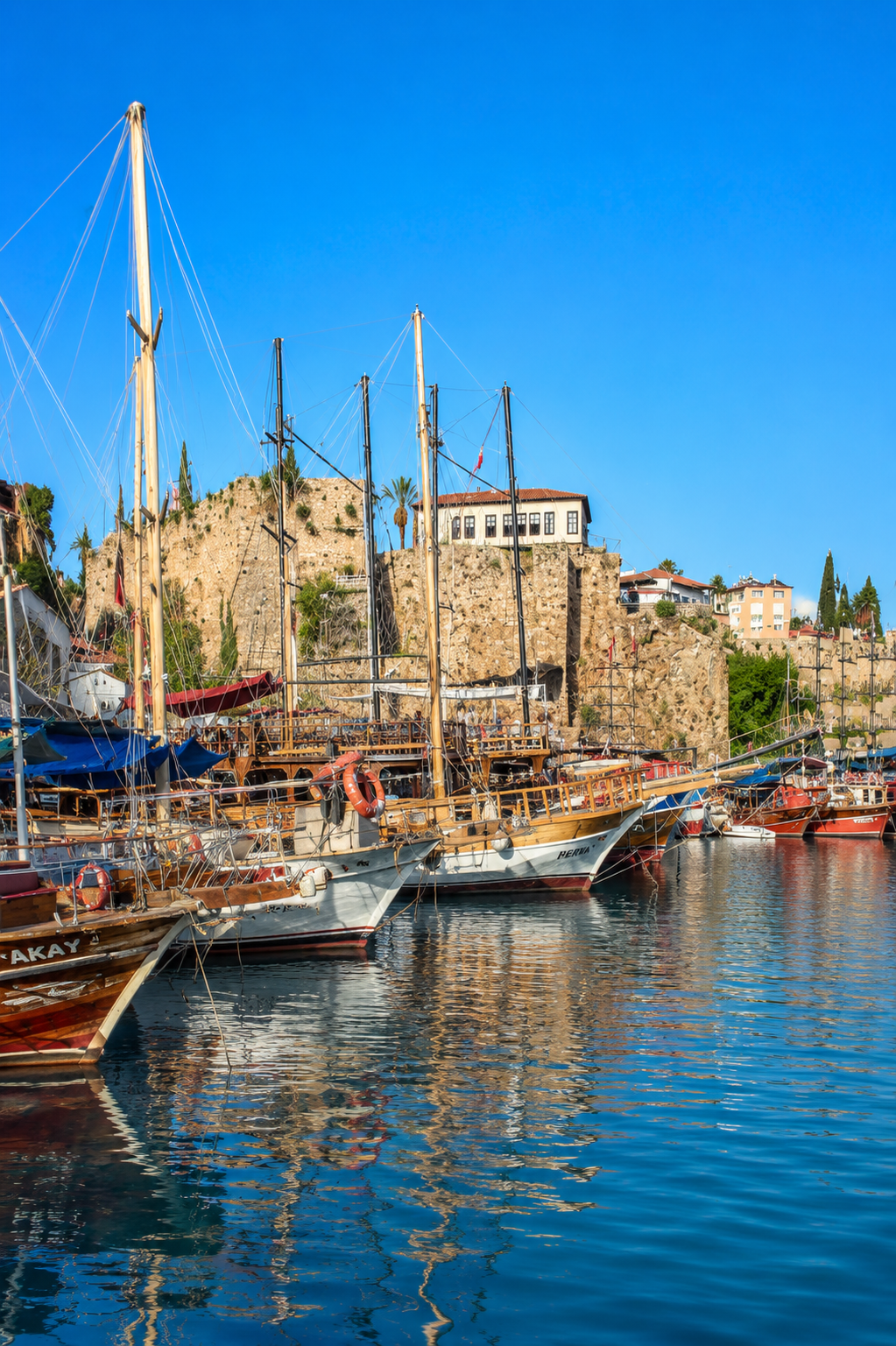 Wooden gulet boats moored in Kaleiçi's old harbour beneath Antalya's Roman city walls