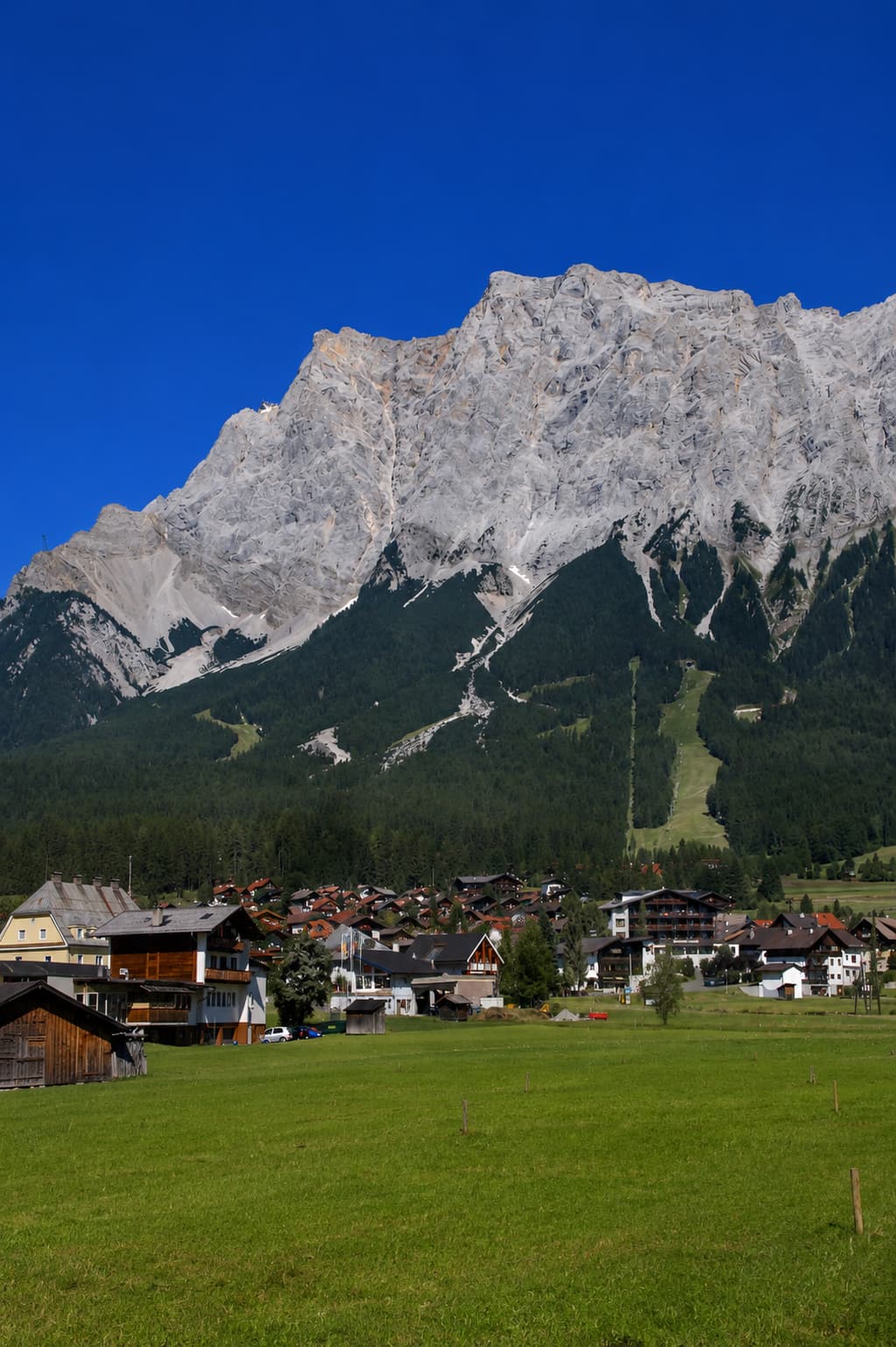 Bavarian village in a green meadow below the steep grey rock face of the Zugspitze near Garmisch-Partenkirchen, Germany