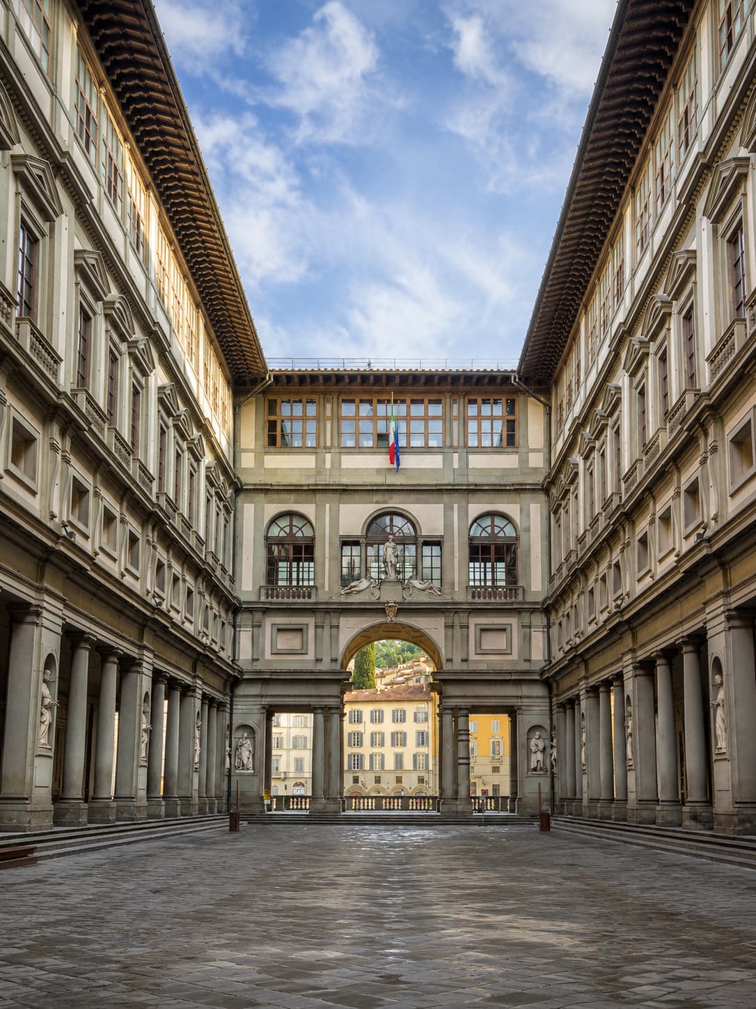 The colonnaded courtyard of the Uffizi Gallery in Florence, statues in niches, framing the arch toward the Arno