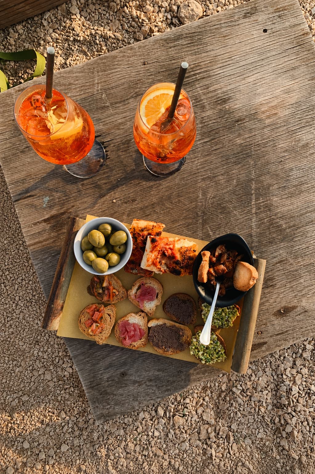 A Florentine aperitivo in golden evening light — two Aperol spritzes and a board of crostini, olives, and small bites on a weathered wooden table