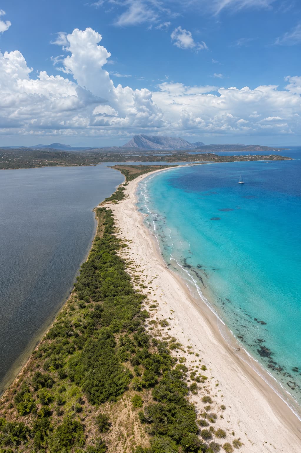 The long white sandbar of La Cinta beach at San Teodoro dividing a lagoon from turquoise sea, with Tavolara island on the horizon