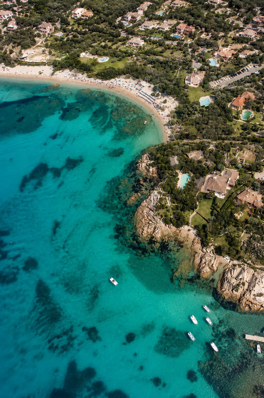 Aerial view of Costa Smeralda villas, granite headland and boats moored over clear turquoise water in northern Sardinia