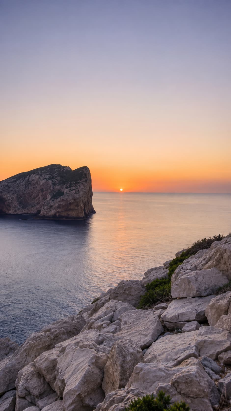 Sunset over calm sea with a rocky headland silhouette on the northern Sardinia coast near Alghero