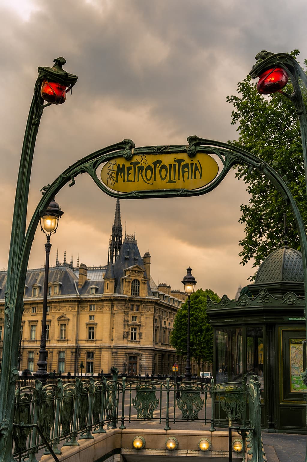 An Art Nouveau Metropolitain sign marking a Paris metro entrance, with the Conciergerie spire in the background