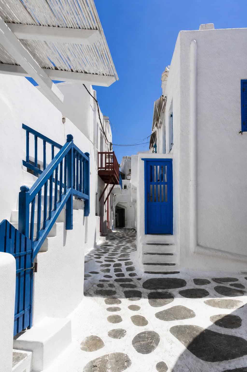 Whitewashed Mykonos lane with blue railings and black-pebble paving in Chora town