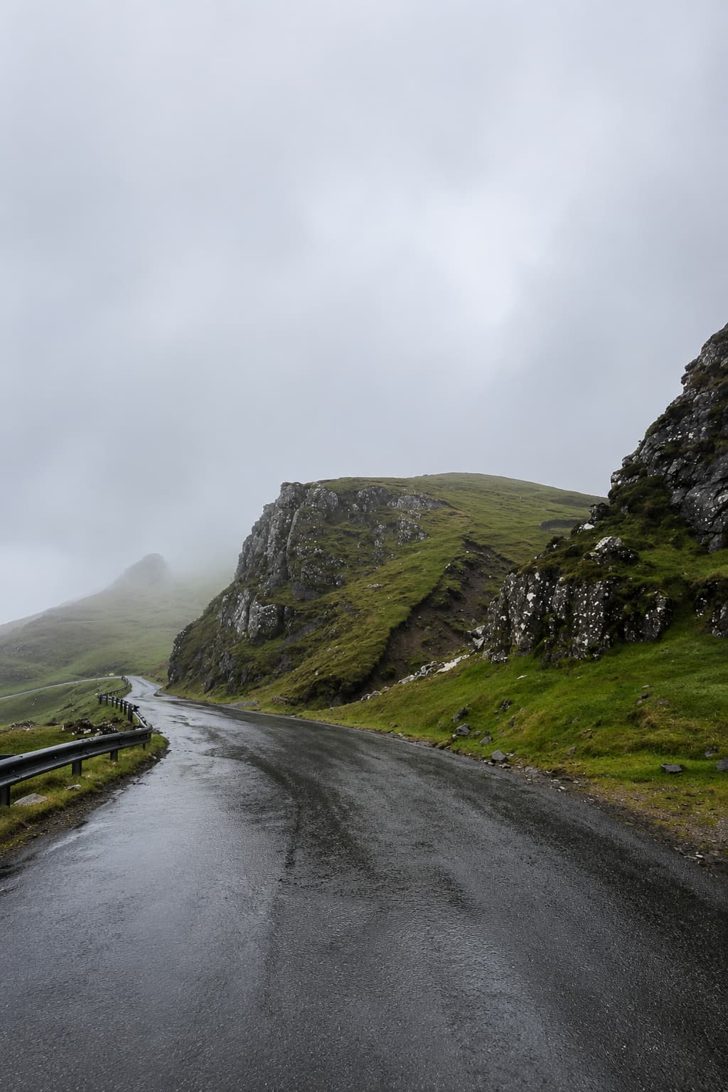 A wet single-track road disappearing into low cloud and mist in the Scottish Highlands