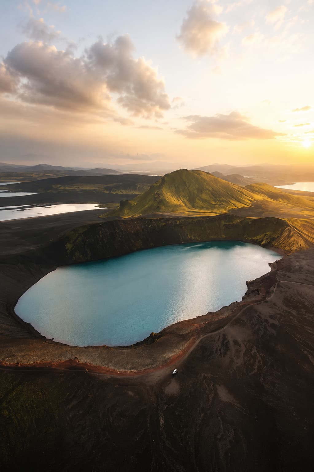 A turquoise crater lake at sunset in a volcanic highland landscape