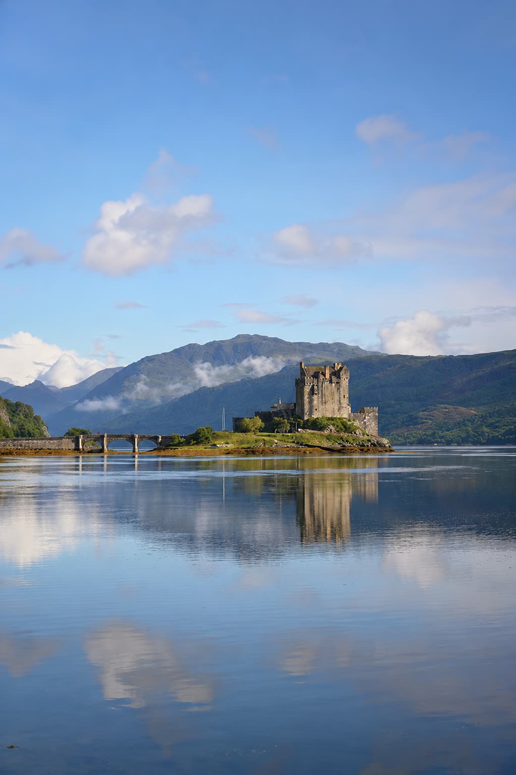 Eilean Donan Castle reflected in still water beneath blue skies in the Scottish Highlands