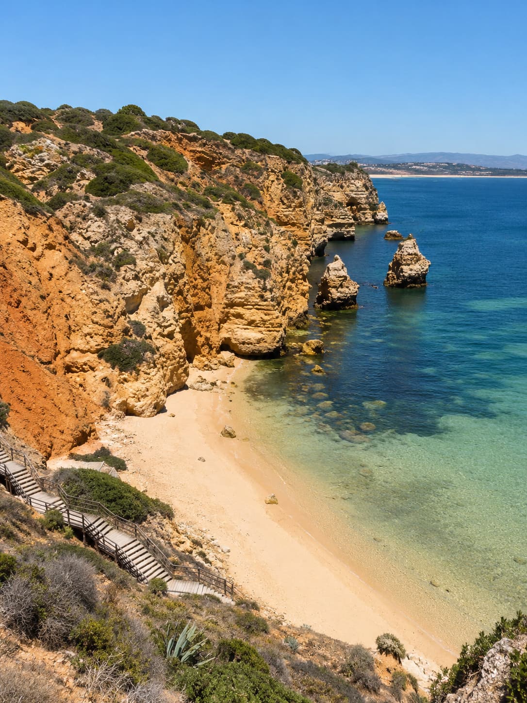 Wooden staircase descending orange sandstone cliffs to a secluded cove on the western Algarve coast near Lagos, Portugal, with turquoise Atlantic water below