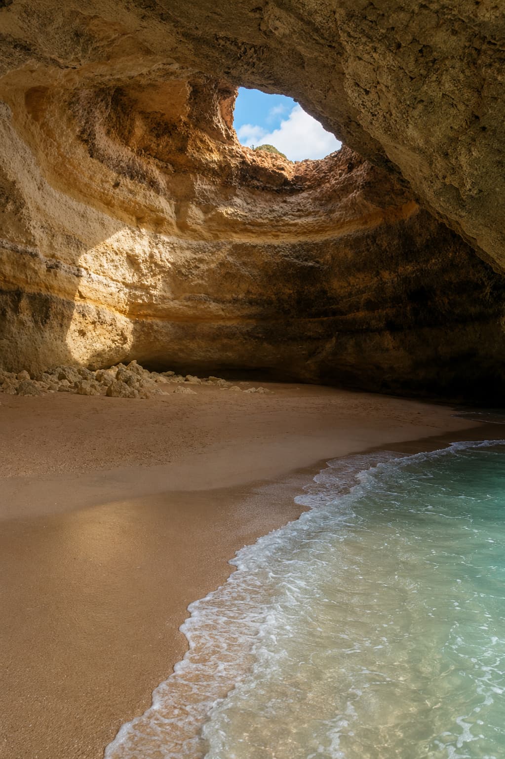 Interior of Benagil Cave in the Algarve, Portugal, showing the natural circular skylight opening in the cave ceiling above the sandy inner beach with clear turquoise water