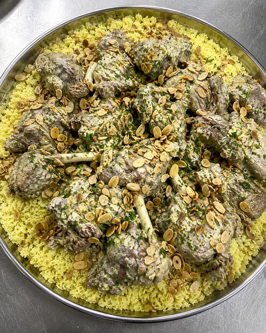 A large shared platter of mansaf — Jordan's national dish of lamb over yellow rice, drizzled with jameed yogurt sauce and scattered with toasted almonds