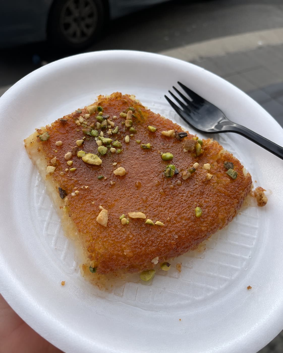 A fresh square of orange-topped kunafa scattered with crushed pistachios on a plate — the cheese pastry Amman is known for