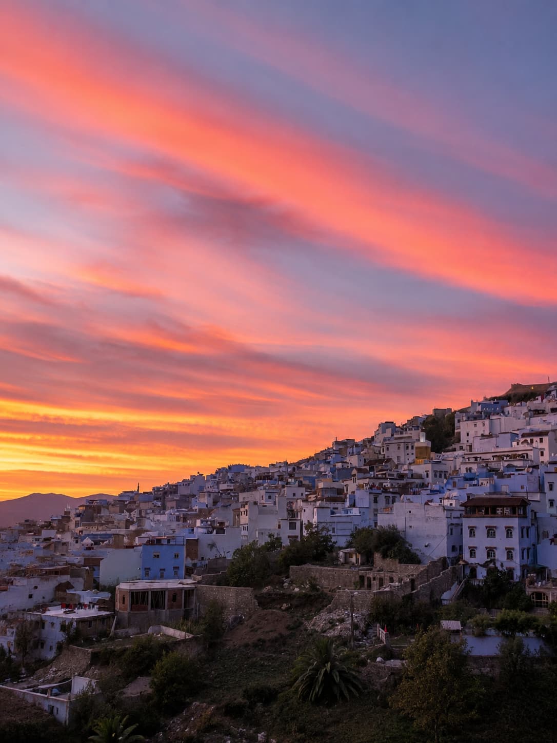 Chefchaouen at sunset with dramatic pink and orange sky streaking above the blue-and-white hillside town