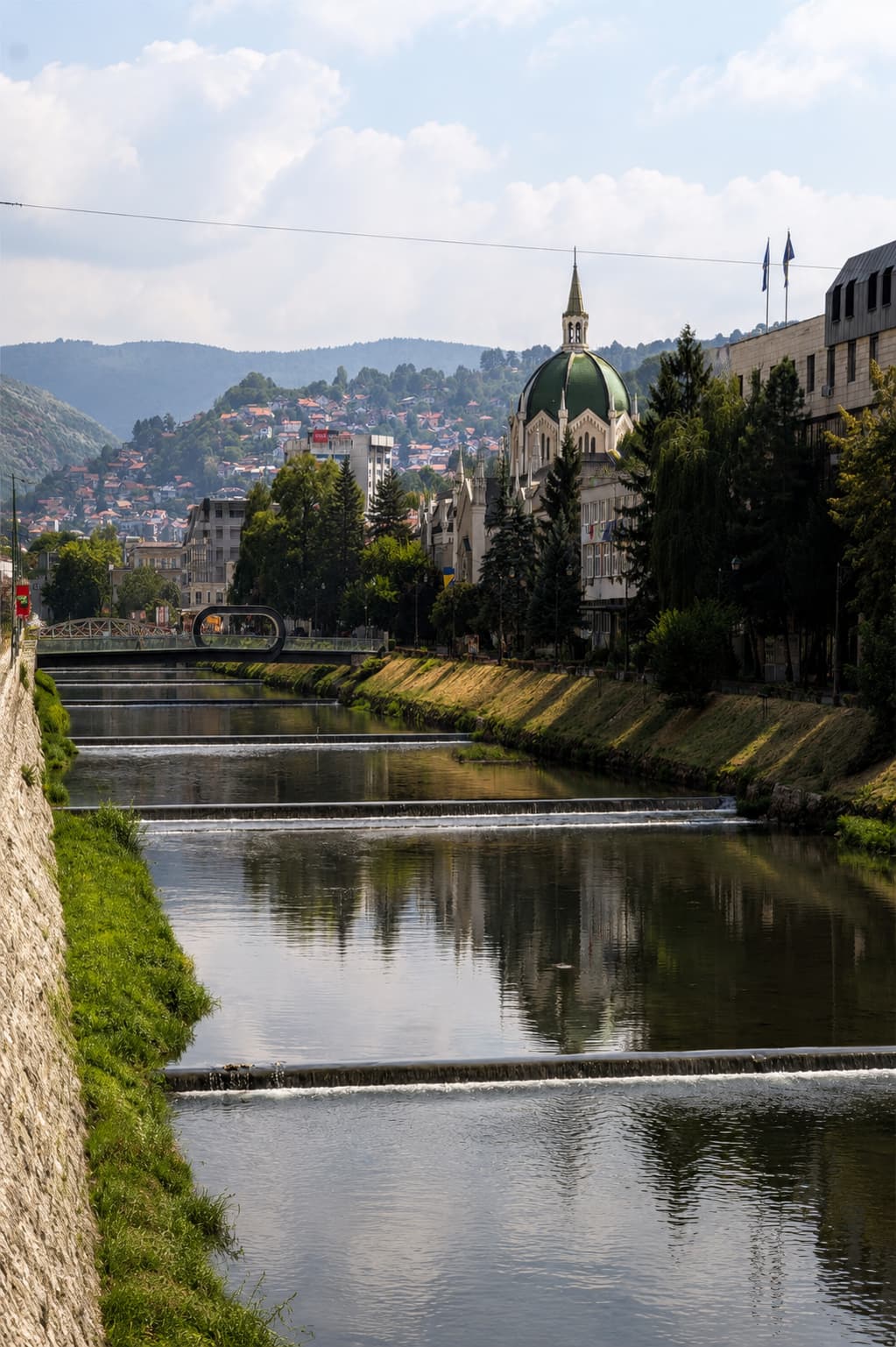 The Miljacka river running through Sarajevo, Bosnia, with the green-domed Ashkenazi Synagogue and hillside neighbourhoods rising behind it