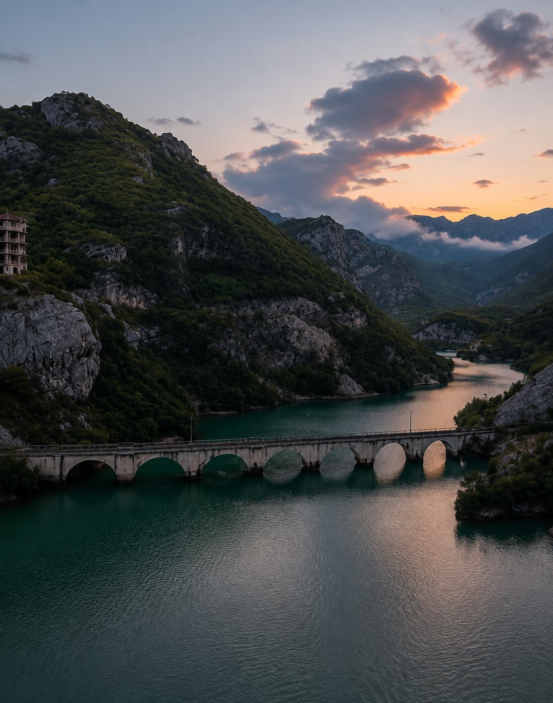 A stone arch bridge crossing a turquoise river gorge in Montenegro at sunset, surrounded by forested limestone cliffs — eastern europe travel by road through the Balkans