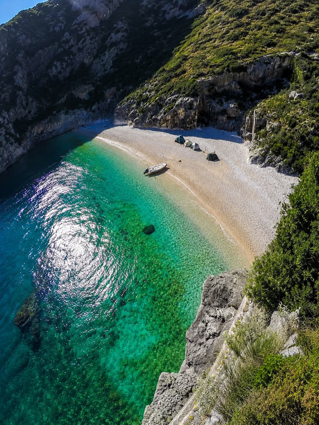 Aerial view of a secluded cove on the Albanian Riviera with turquoise water, a white pebble beach, and two tents — eastern europe travel on the Adriatic coast