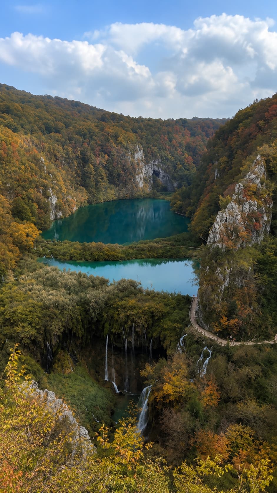 Plitvice Lakes National Park in Croatia in autumn, turquoise terraced lakes surrounded by orange and gold fall foliage on the hillsides, waterfalls and wooden walkways visible below