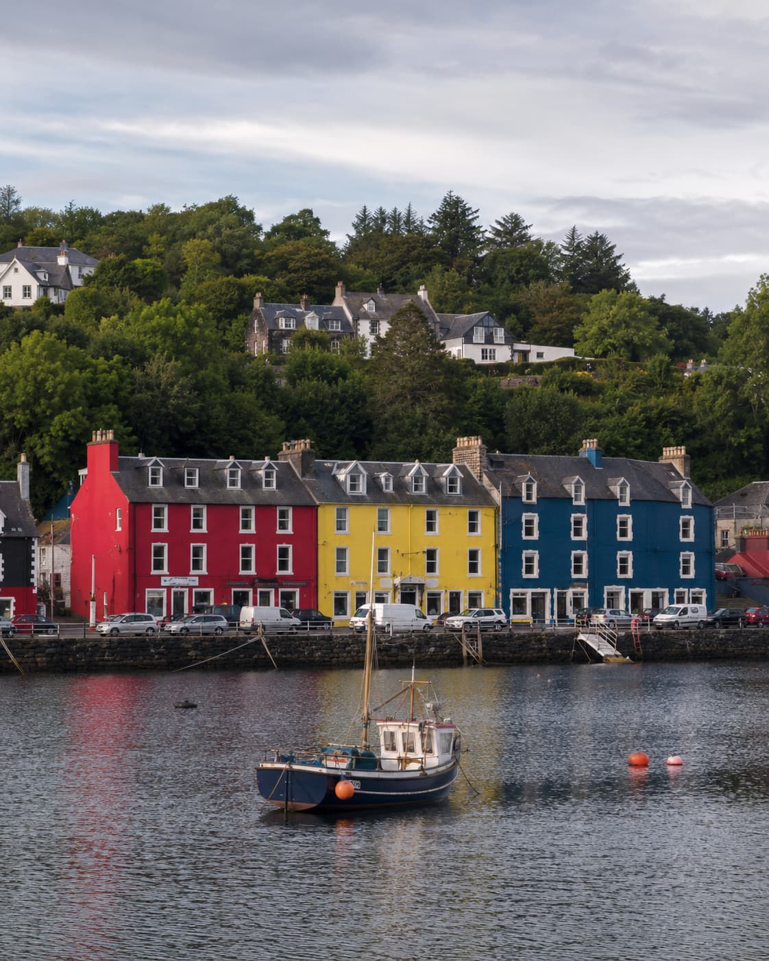 Tobermory harbour — colourful painted houses in red, yellow and blue reflected in the bay, fishing boat in the foreground, Isle of Mull Scotland