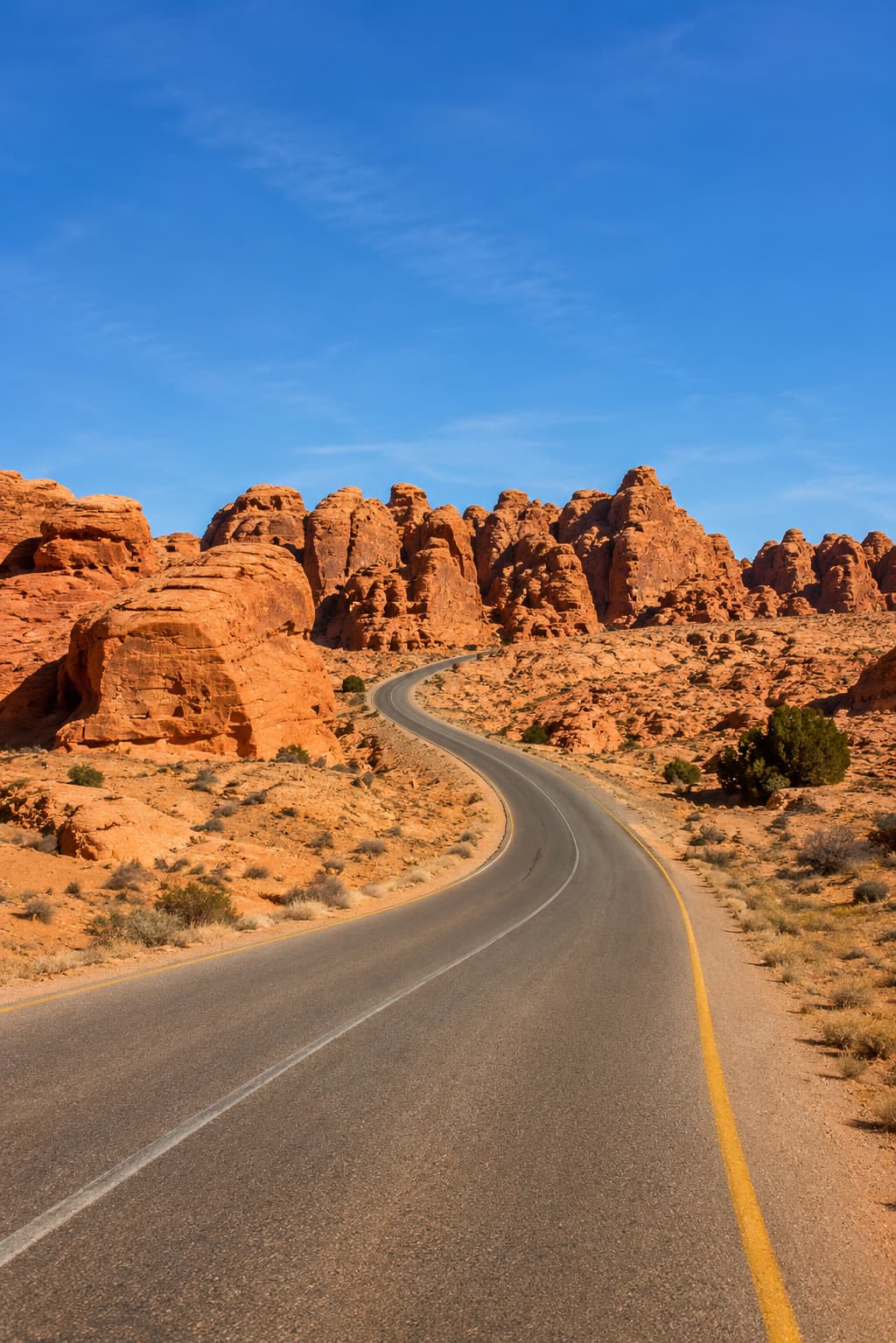 A winding paved desert road through red sandstone rock formations on a Jordan road trip