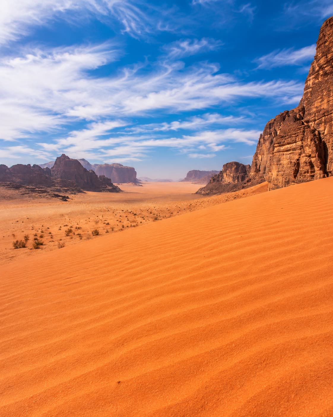 Red sand dune and sandstone massifs in Wadi Rum desert under a blue sky