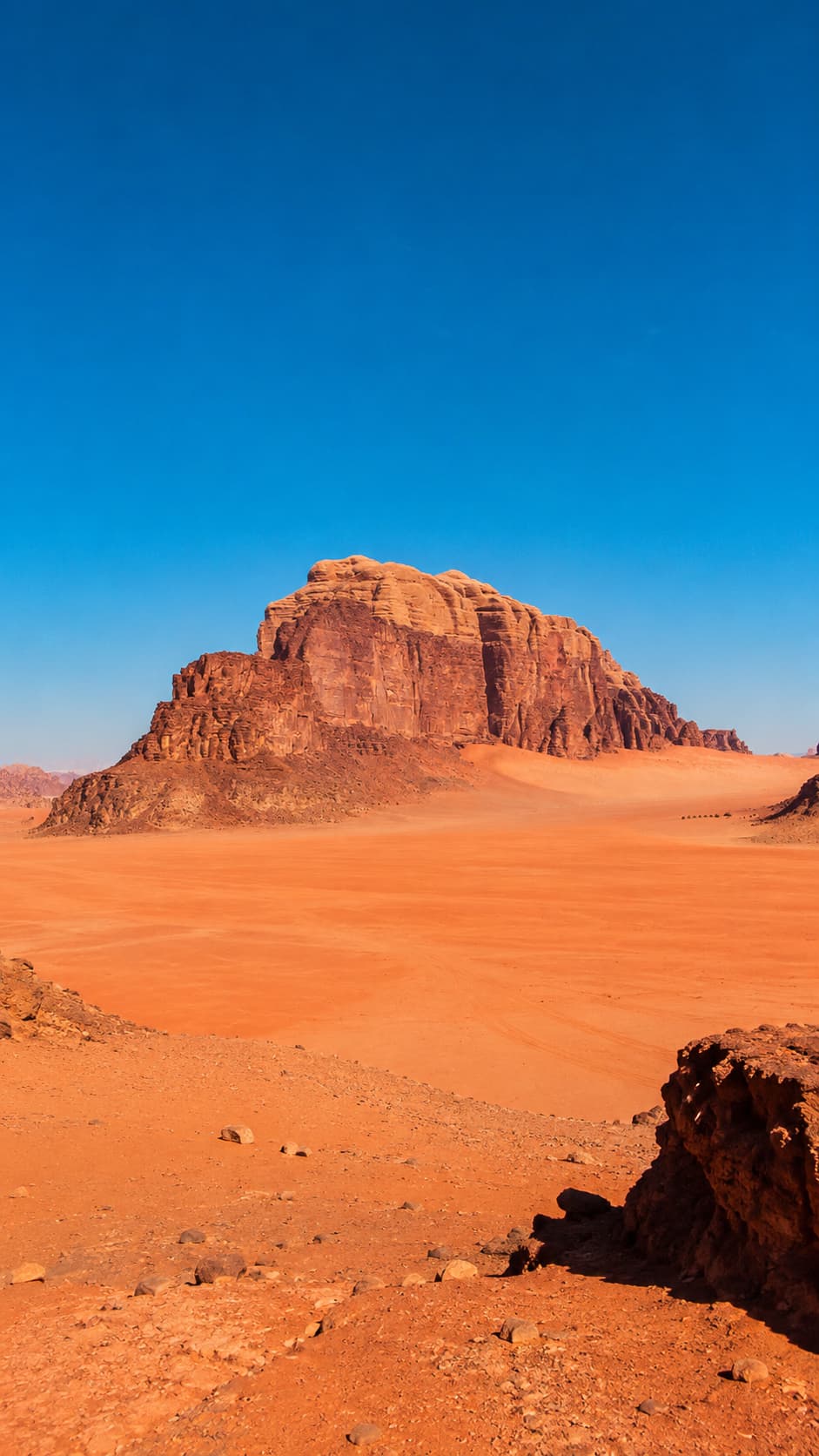 A lone sandstone mountain rising from the red desert floor of Wadi Rum