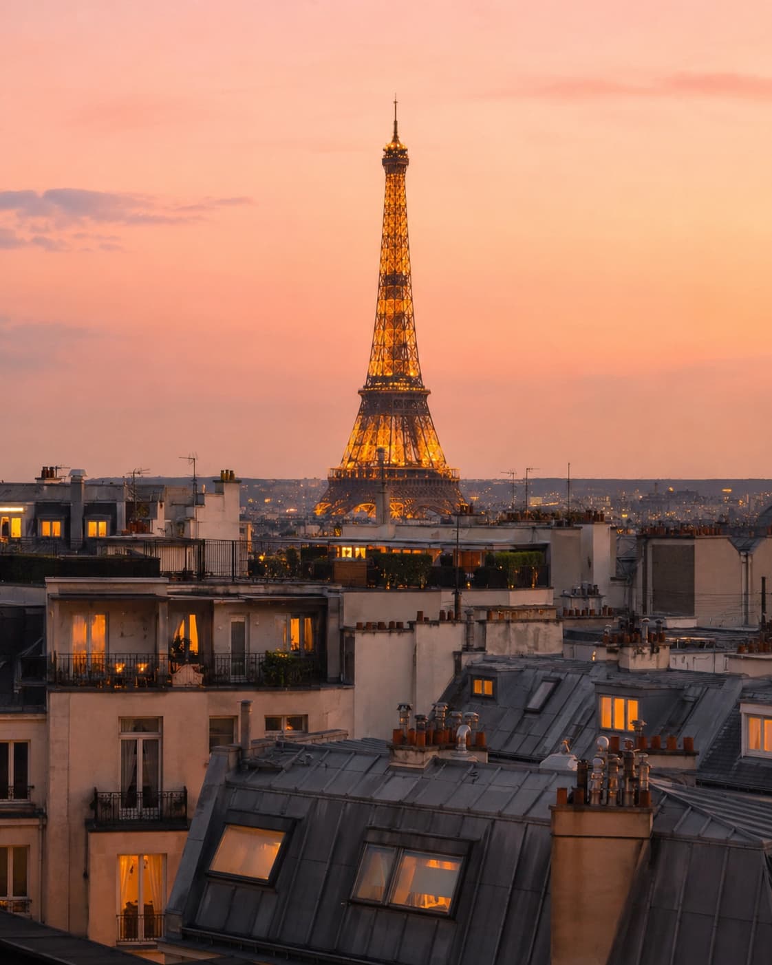 The illuminated Eiffel Tower glowing gold above Paris rooftops at sunset with a pink and orange sky — July is one of the best times to visit for long evenings and Bastille Day