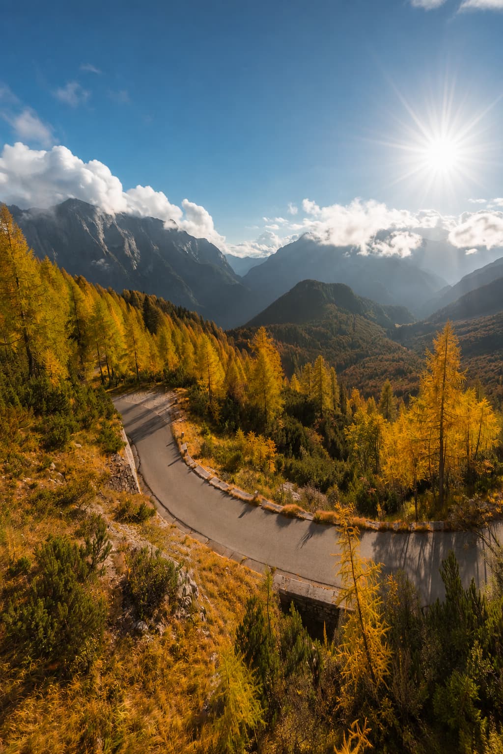 Winding mountain road through golden larch forest in the Julian Alps, Slovenia — the autumn colour on the Lake Bled autumn itinerary day-trip route toward the Vršič Pass