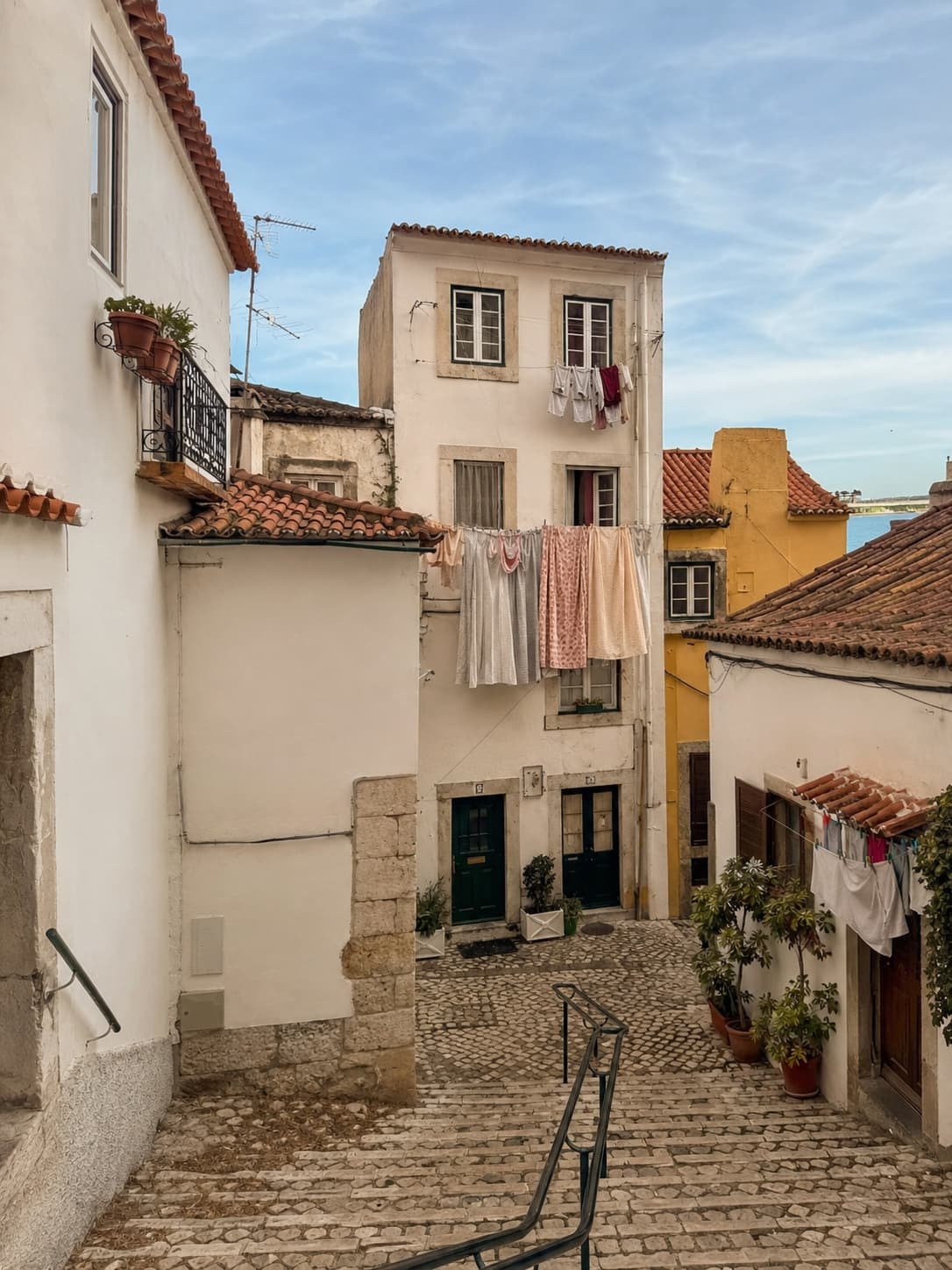 Cobblestone steps descending through Alfama Lisbon with laundry lines strung between whitewashed buildings