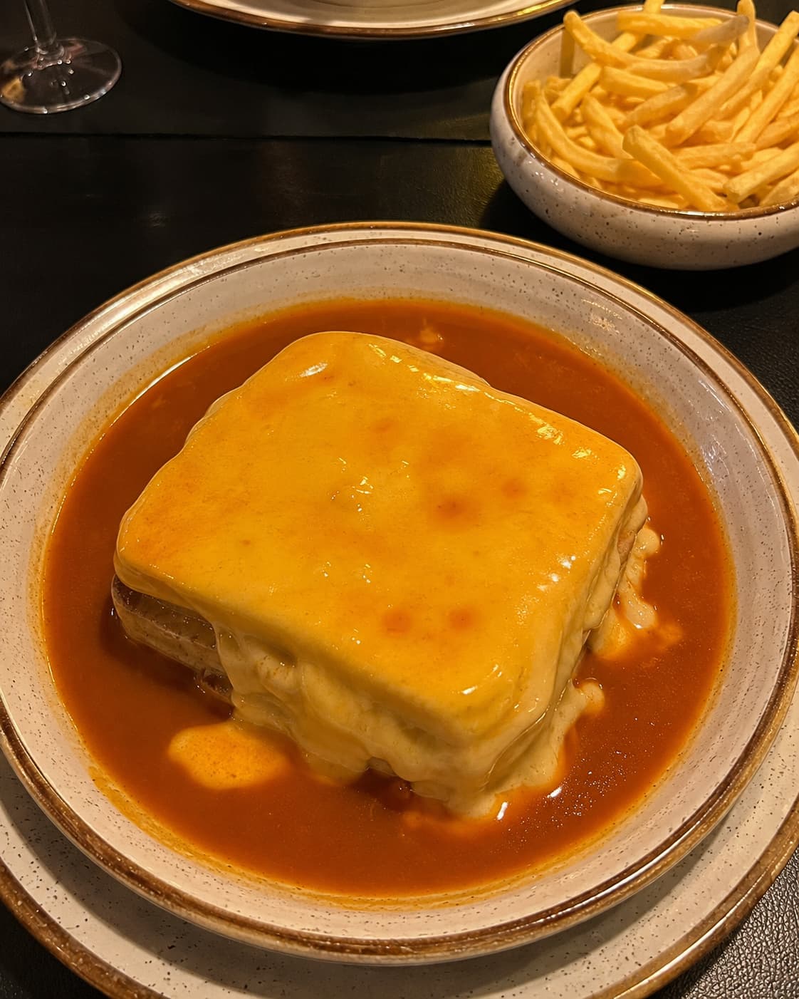 A francesinha — Porto's signature layered meat sandwich — served in a deep tomato and beer sauce with a bowl of chips alongside