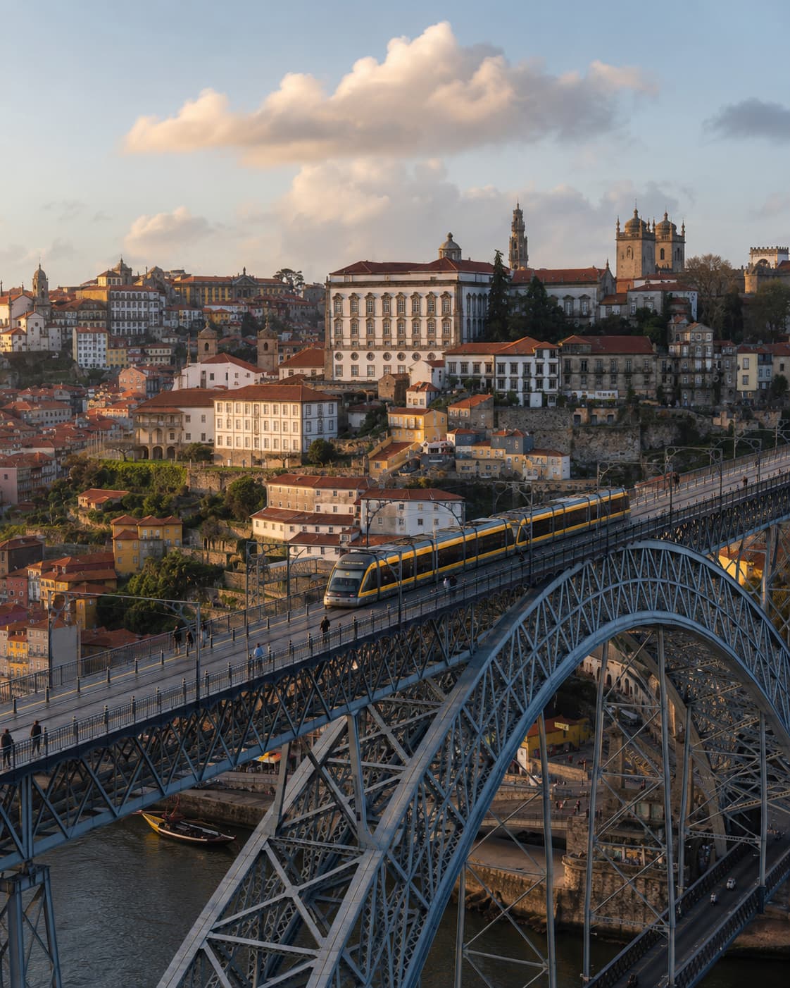Ponte Dom Luís I in Porto at golden hour — a yellow metro train crosses the upper iron deck with the historic city and church towers rising behind