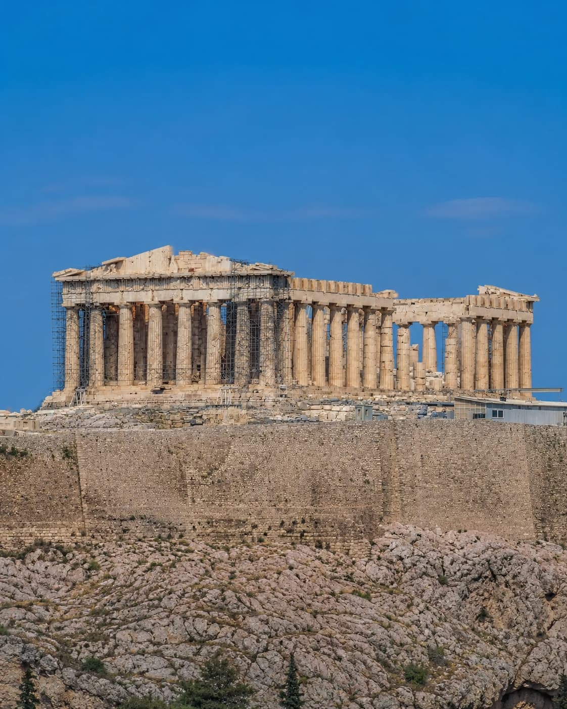 The Parthenon on the Acropolis in Athens under a deep blue August sky — the ancient limestone monument fully exposed on its hill with no shade, the surrounding rock bleached white by the sun, illustrating why Athens in August is one of the Mediterranean's most demanding heat experiences.