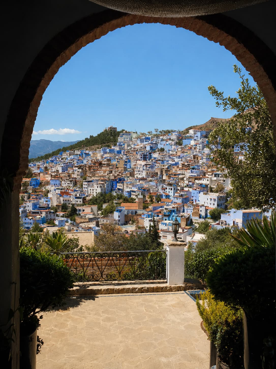 Chefchaouen viewed through a stone arch — the blue and white hilltop city spread across the Rif Mountains under a clear sky