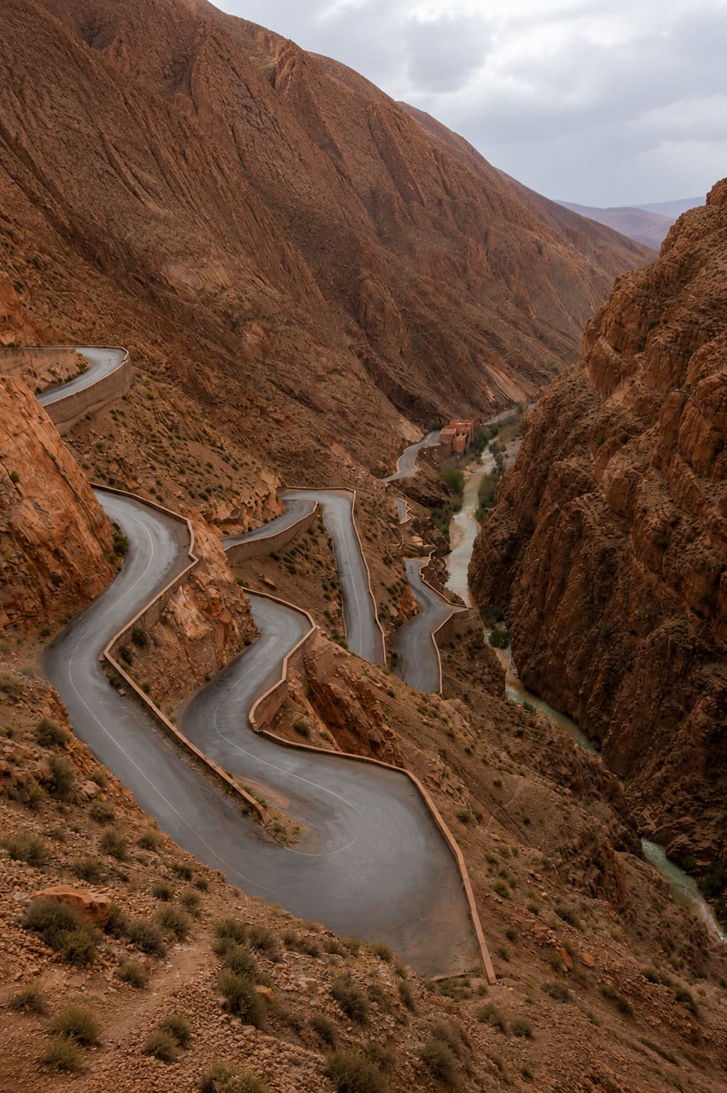 The Dades Gorge road in Morocco — dramatic zigzag switchbacks carved into sheer red canyon walls, a river running at the bottom
