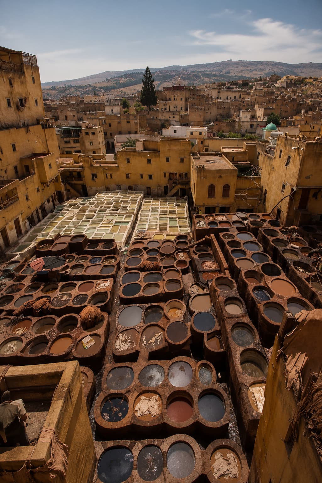 Chouara tannery in Fes seen from above — circular dye vats in earth tones surrounded by the old medina rooftops