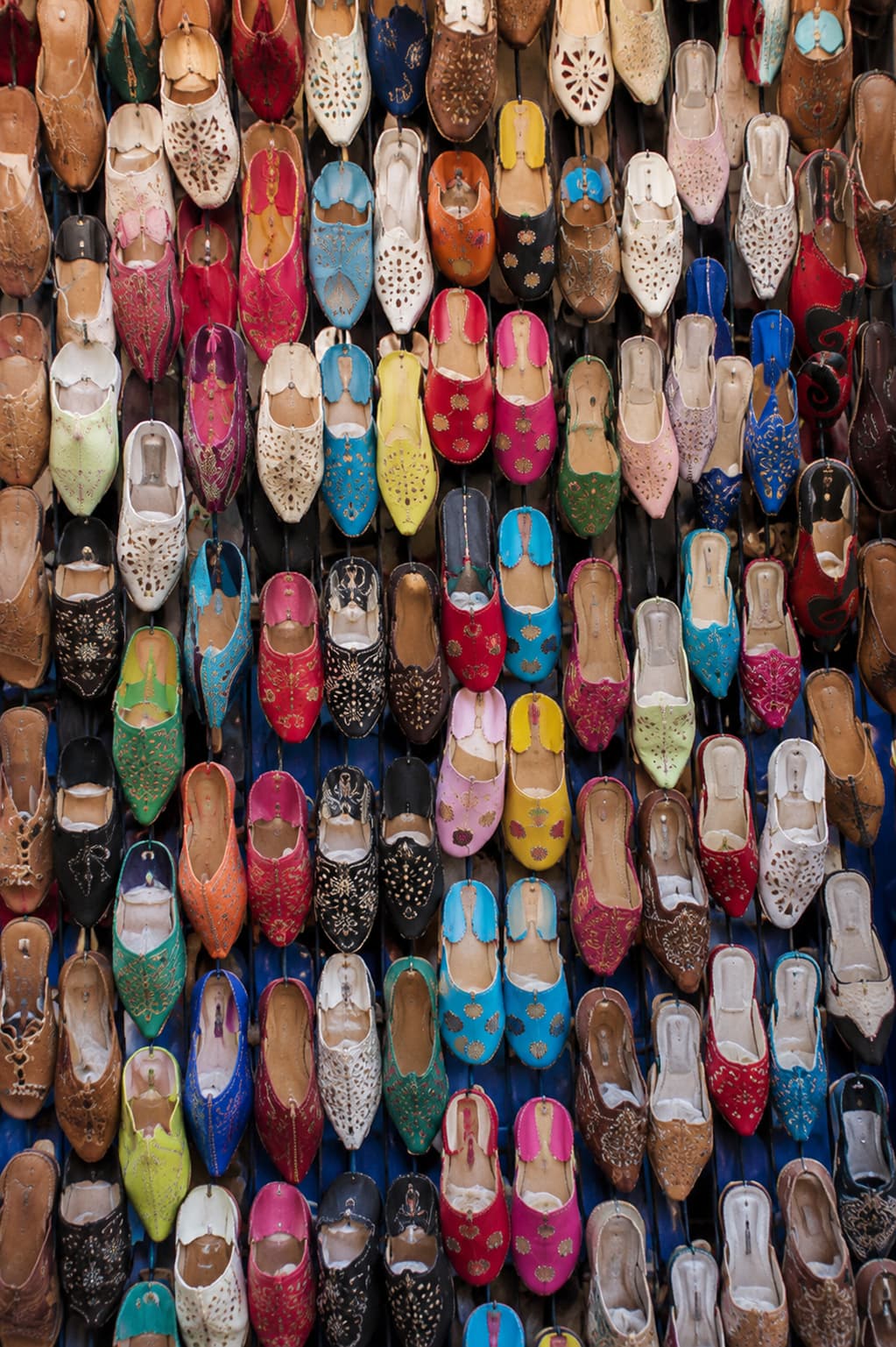 Wall of colourful Moroccan babouches leather slippers in a souk — rows of embroidered shoes in pink, blue, red, and gold