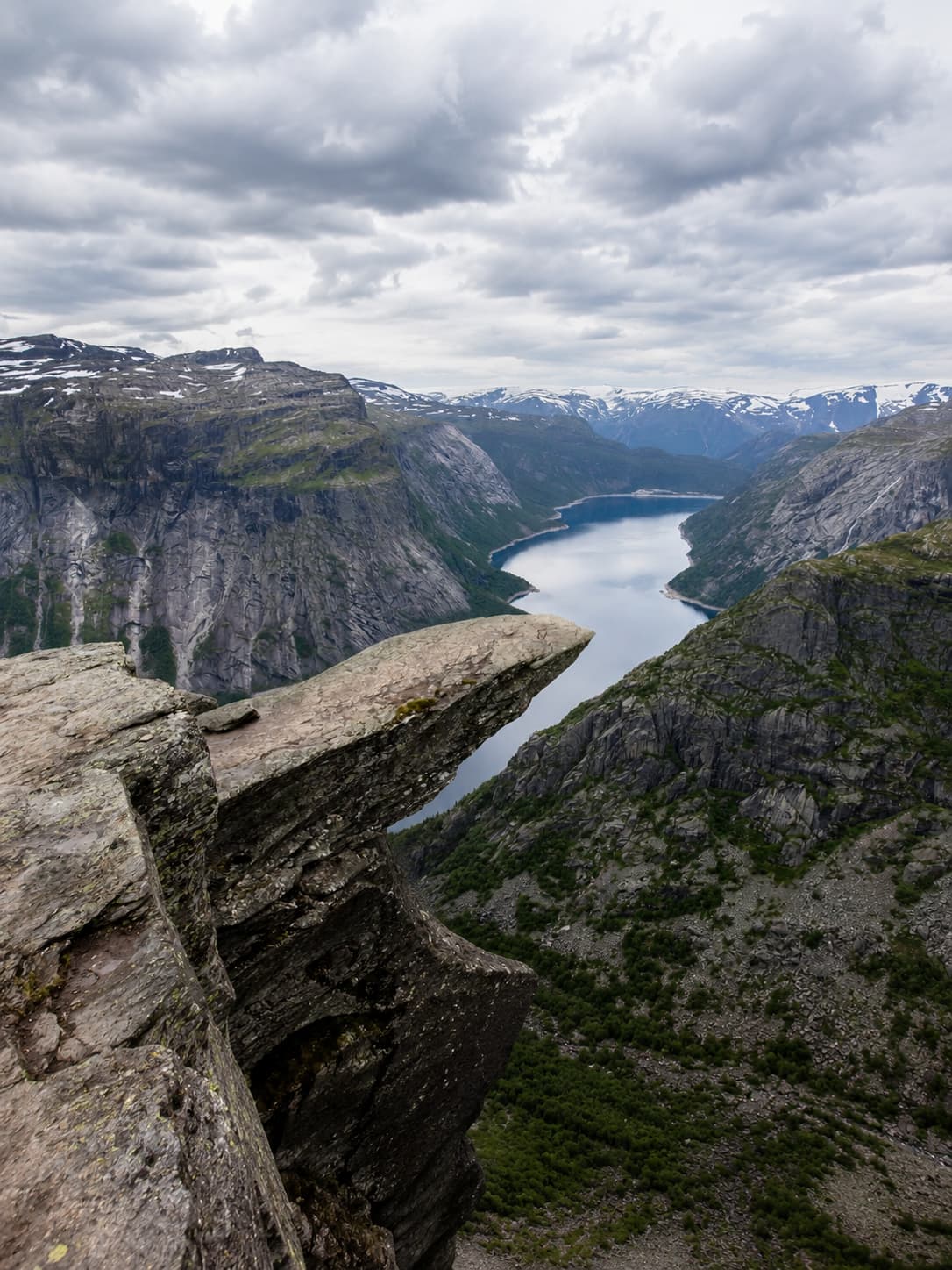 View from Trolltunga rock ledge over the Hardangerfjord, steep cliff walls and a winding blue fjord stretching into snow-capped mountains beyond