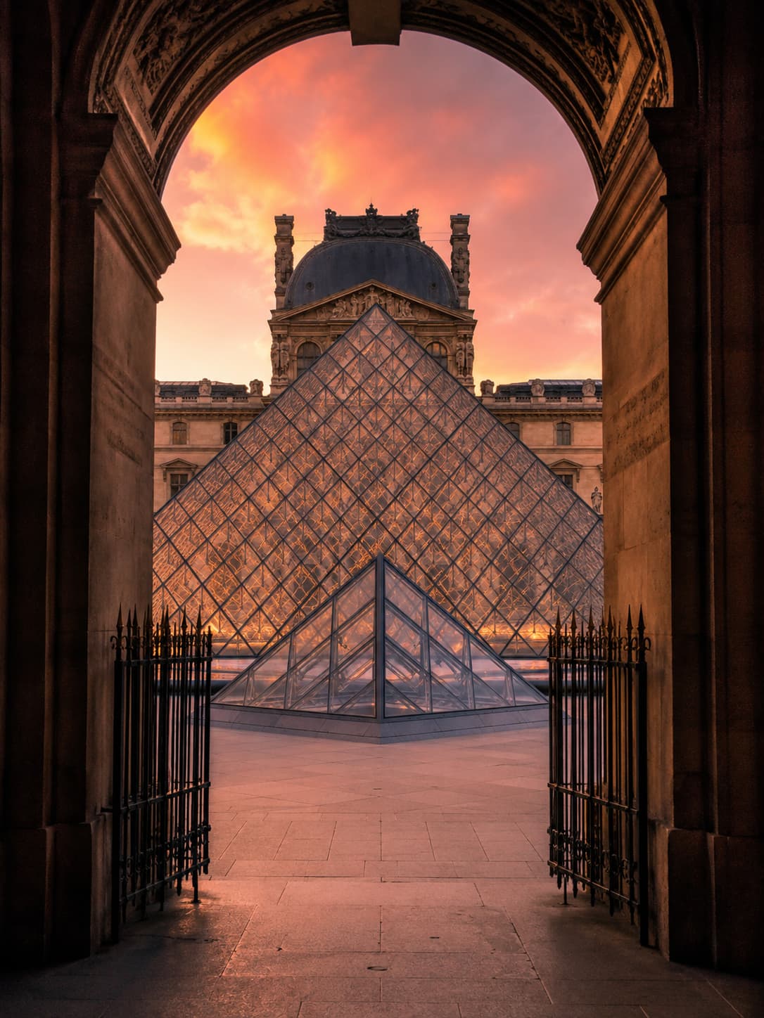 Louvre glass pyramid framed through a stone archway at sunset, Paris