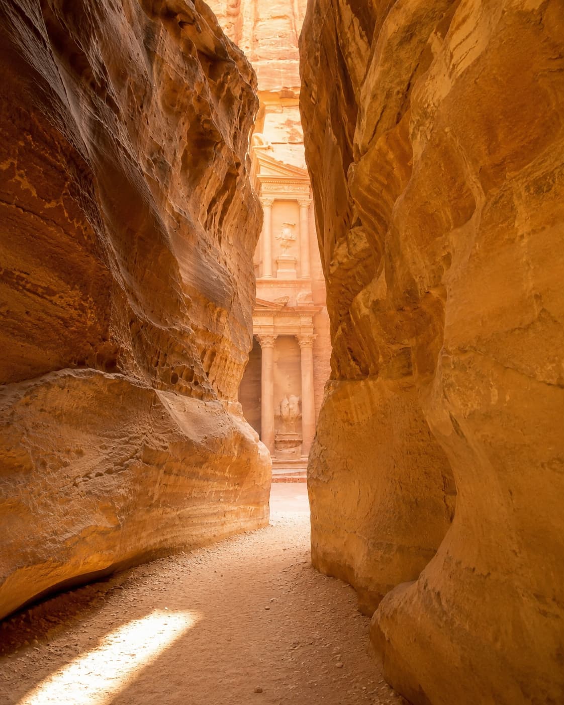Petra travel tips — the Treasury glowing at the end of the narrow Siq canyon, warm morning light on rose-pink stone