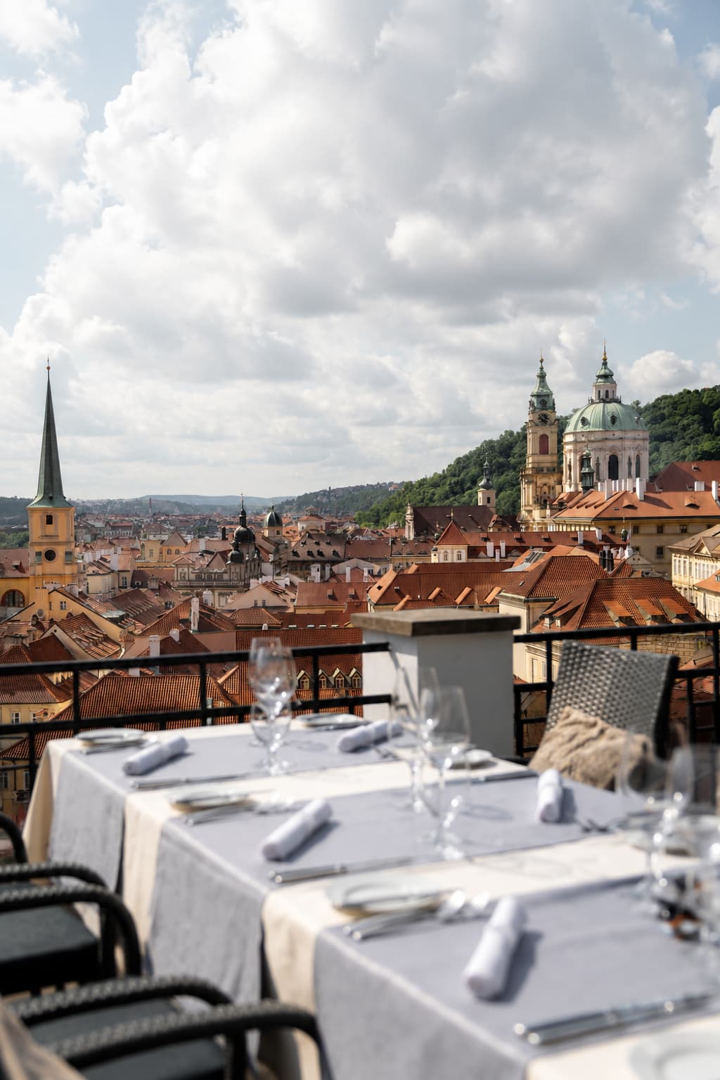 Rooftop restaurant terrace in Malá Strana Prague with St. Nicholas church dome and red tile rooftops visible, one of the most beautiful cafe views in Prague