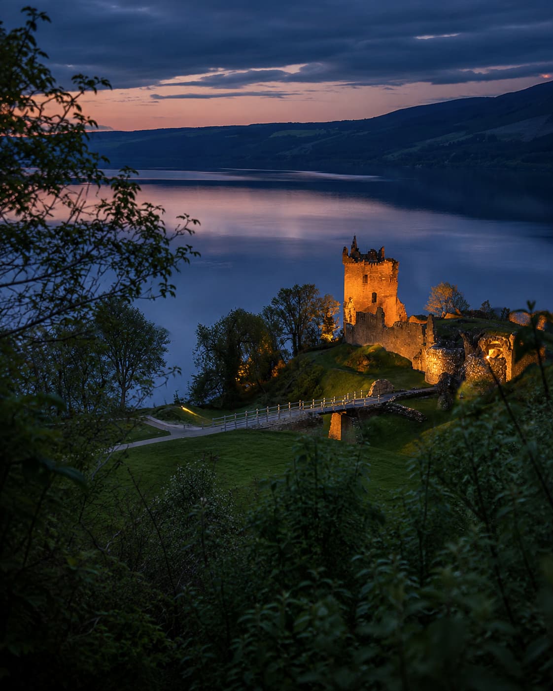 Urquhart Castle lit up at dusk on the shore of Loch Ness, dark purple sky reflected in still water — Day 6 of the Scotland itinerary