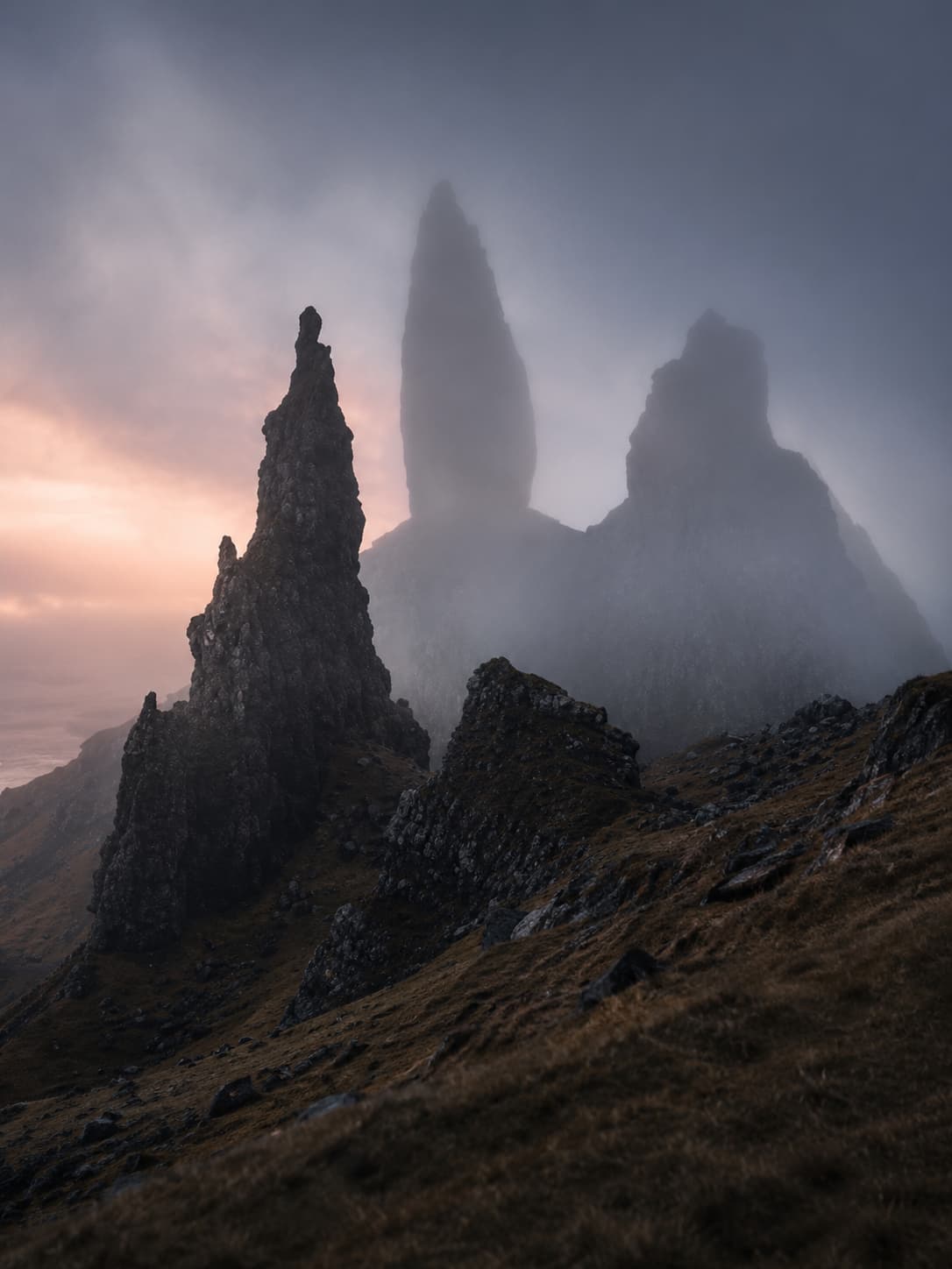 Old Man of Storr on Isle of Skye shrouded in mist at dawn, jagged rock pinnacles emerging from cloud — the defining image of a Scotland itinerary