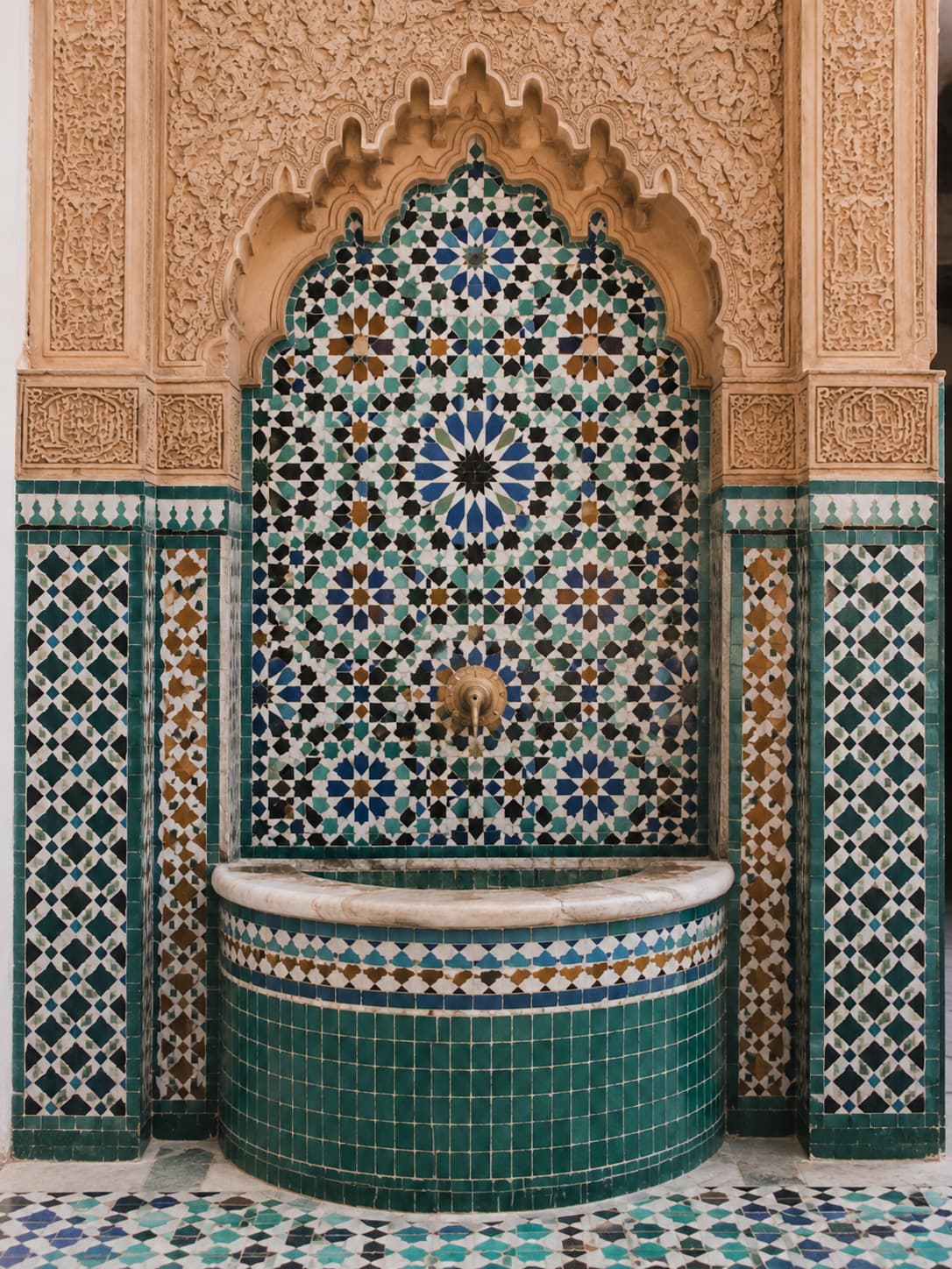 Ornate Moroccan zellige mosaic fountain with geometric tilework and carved stucco arch in a traditional riad