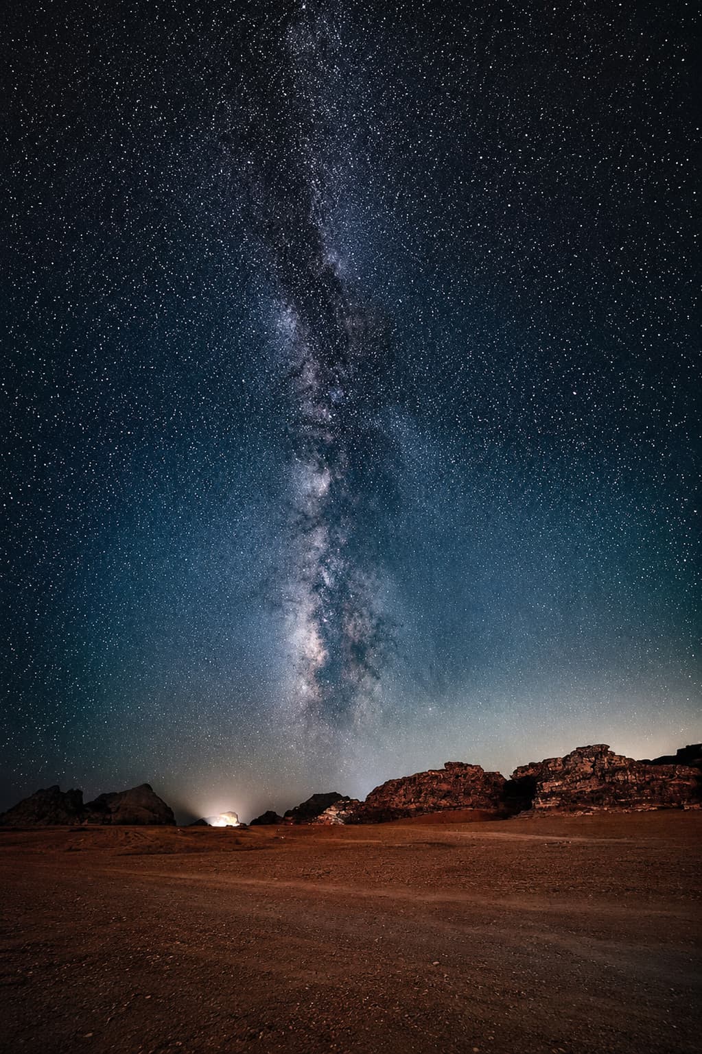 The Milky Way rising above the open Wadi Rum desert floor, sandstone rock formations silhouetted against the night sky
